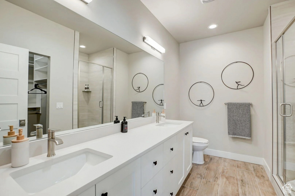 Bathroom featuring a shower with door, double vanity, hardwood / wood-style floors, and toilet