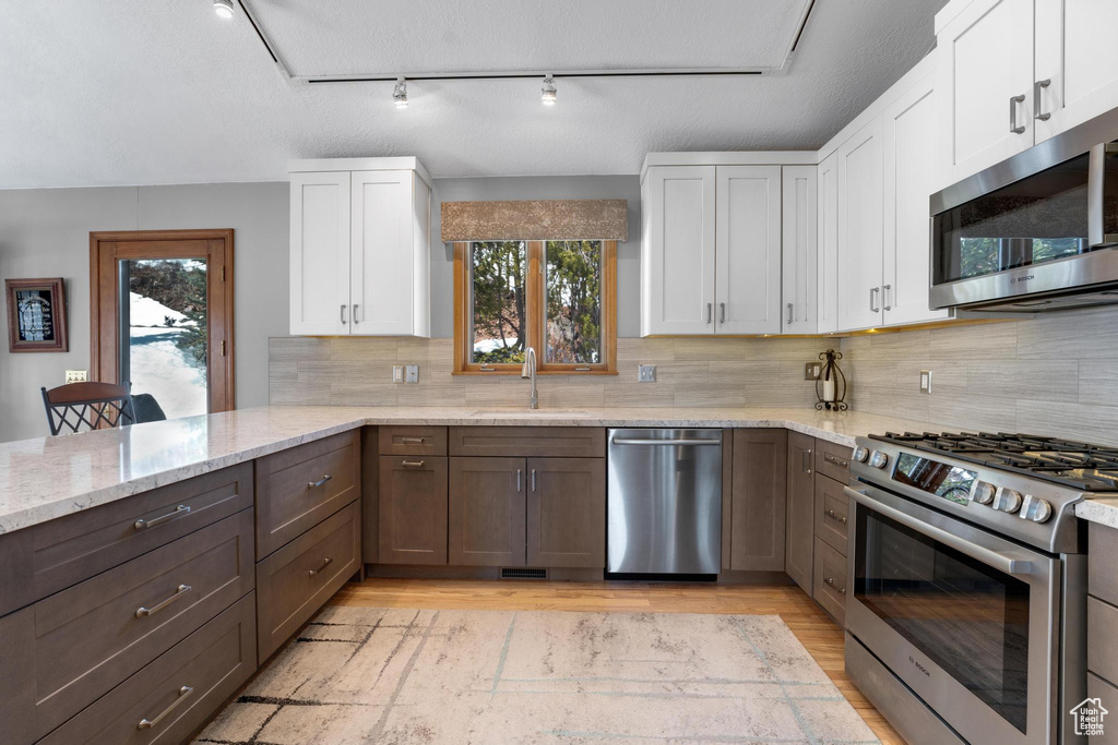Kitchen featuring backsplash, stainless steel appliances, track lighting, light stone countertops, and white cabinetry