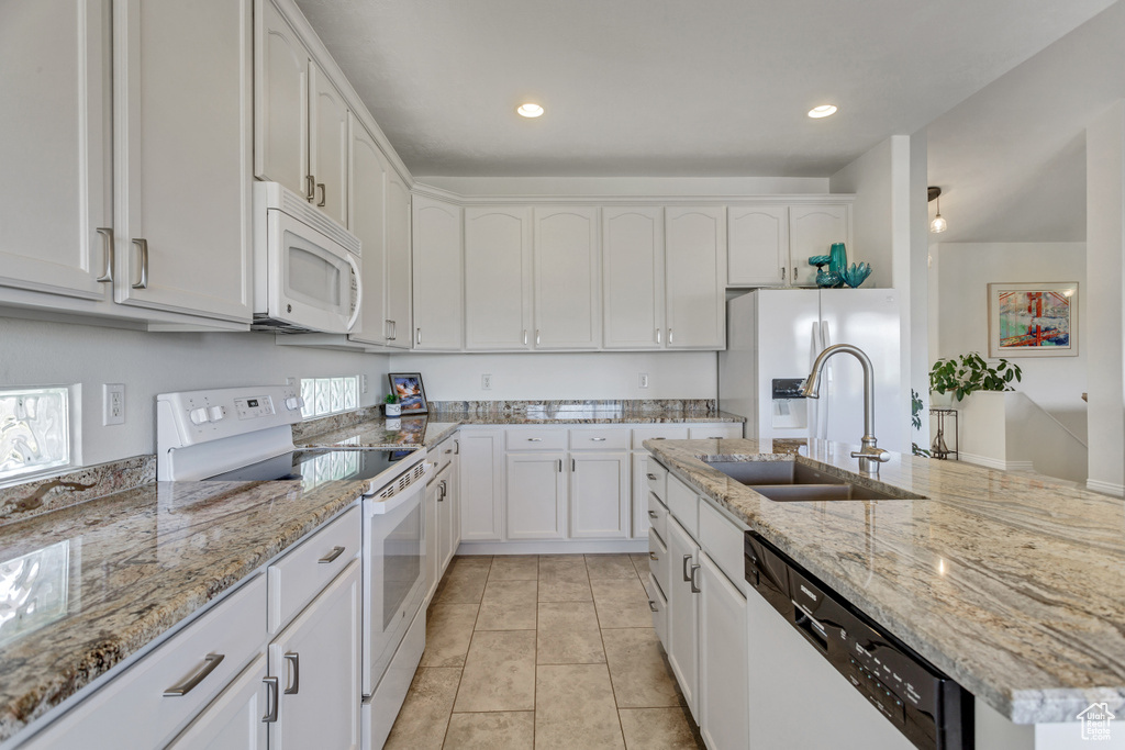 Kitchen featuring white appliances, light tile flooring, light stone counters, white cabinetry, and sink