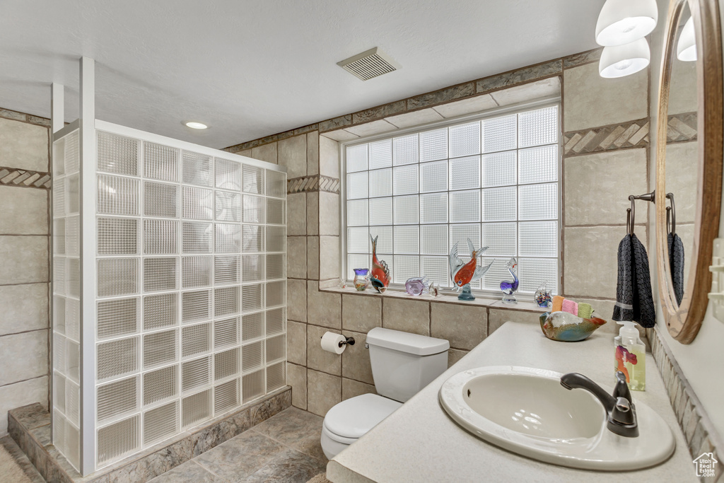 Bathroom featuring tile walls, oversized vanity, a shower, toilet, and tile flooring
