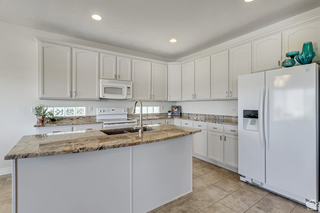 Kitchen with stone counters, white appliances, white cabinets, sink, and light tile floors