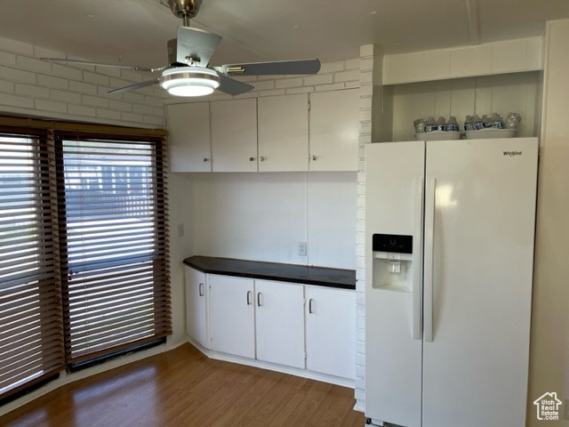 Kitchen featuring wood-type flooring, white refrigerator with ice dispenser, ceiling fan, and white cabinetry
