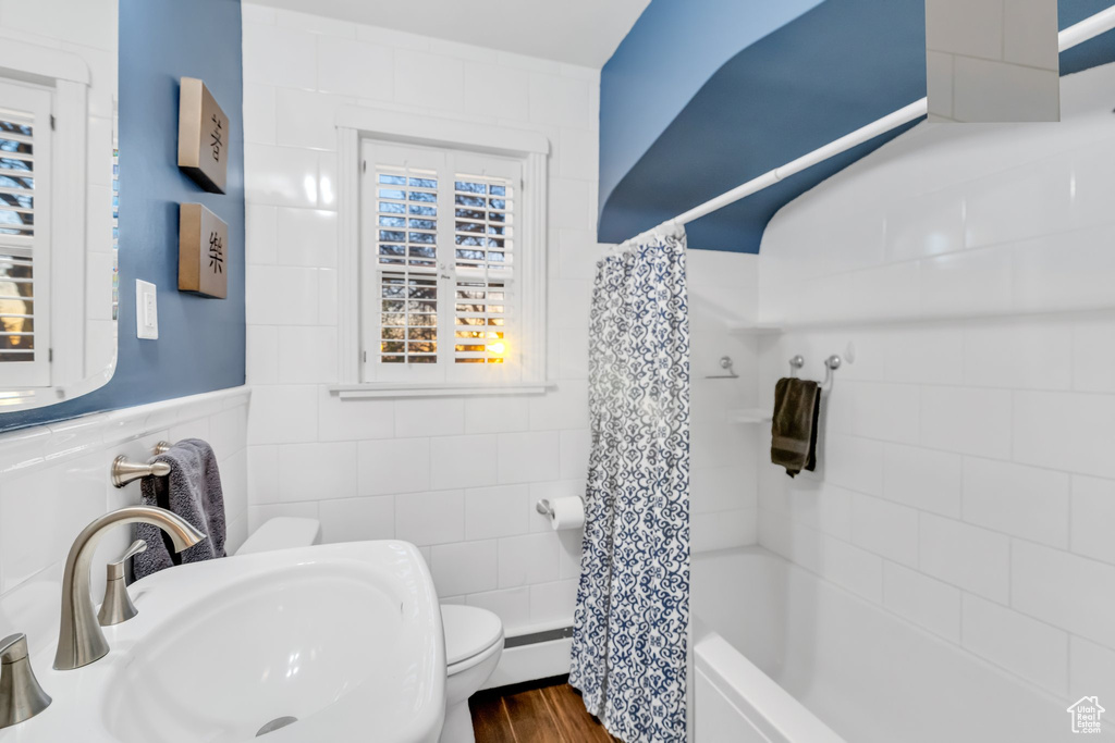 Full bathroom featuring tile walls, shower / bath combo with shower curtain, sink, toilet, and wood-type flooring