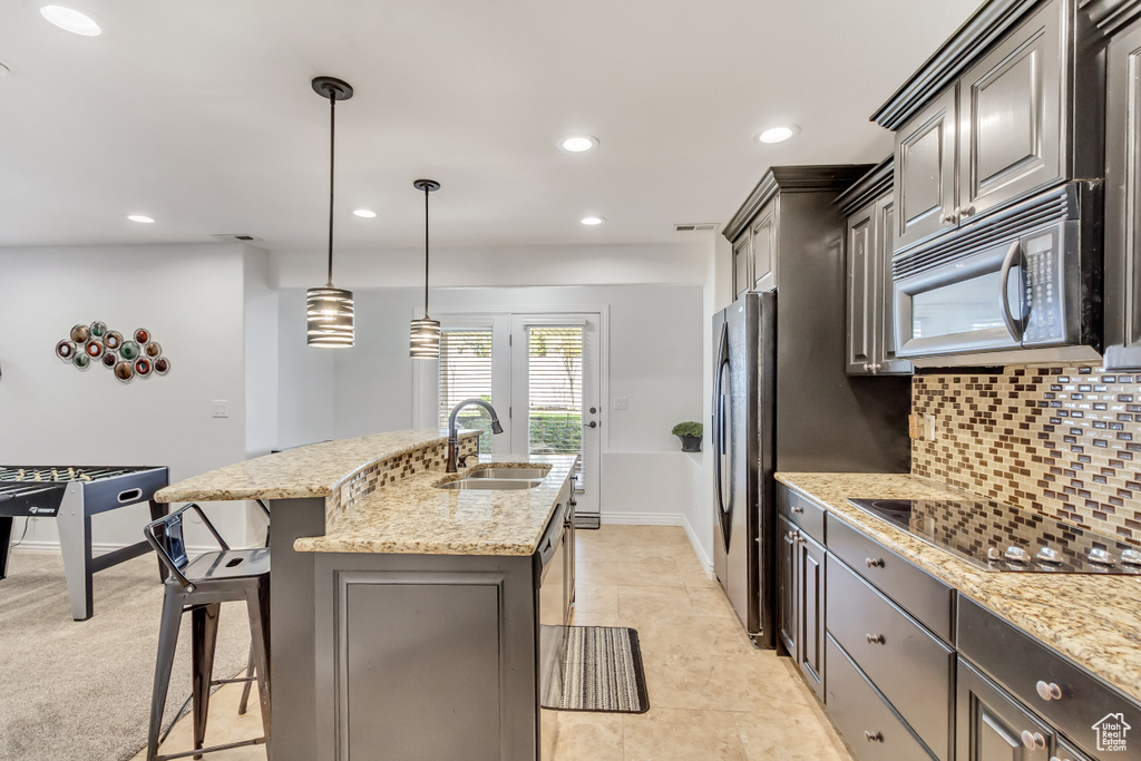 Kitchen featuring sink, backsplash, stainless steel appliances, an island with sink, and pendant lighting