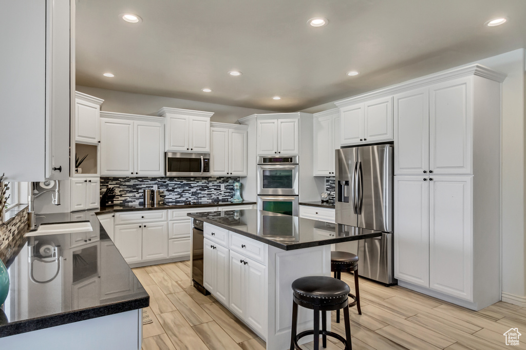 Kitchen with a kitchen island, stainless steel appliances, backsplash, and white cabinetry