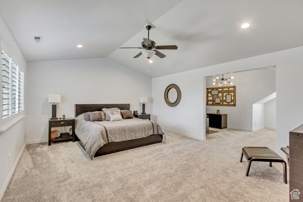 Carpeted bedroom with ceiling fan with notable chandelier and vaulted ceiling