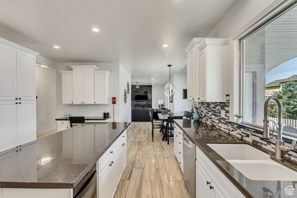 Kitchen with decorative light fixtures, white cabinets, backsplash, a kitchen island, and dark stone countertops
