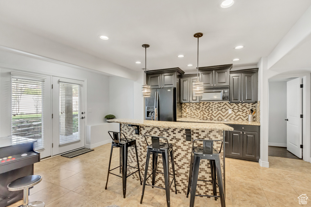 Kitchen with light tile flooring, hanging light fixtures, stainless steel fridge, and a kitchen breakfast bar