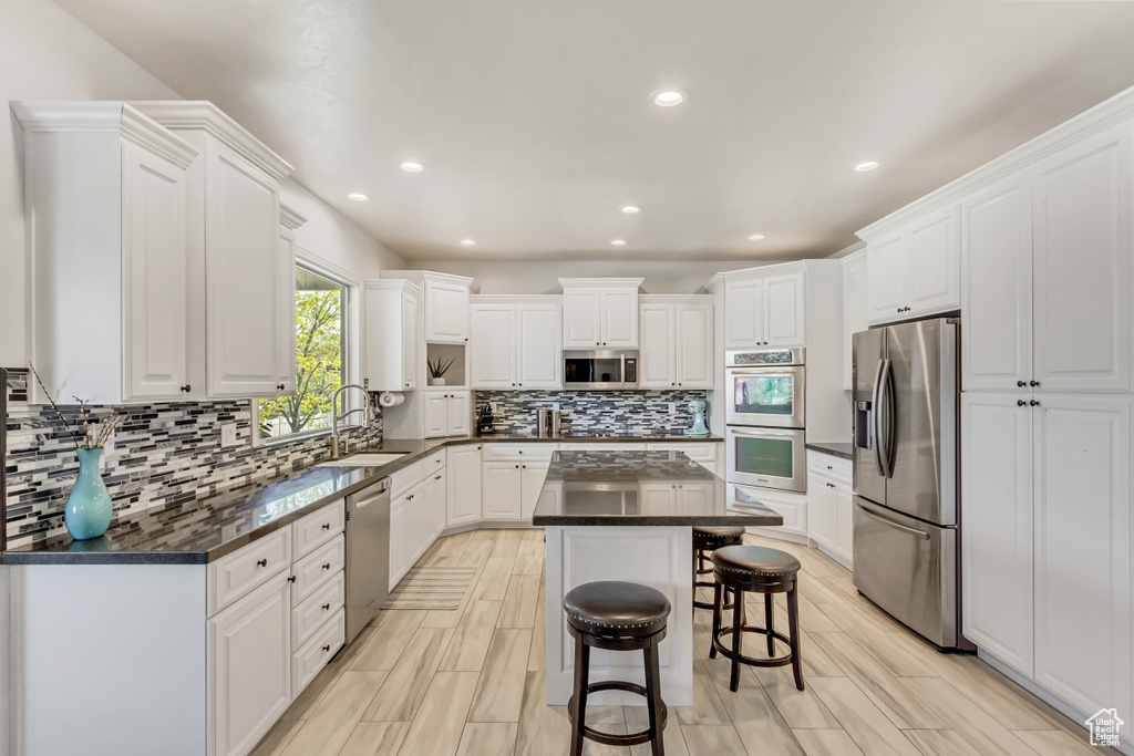 Kitchen featuring white cabinetry, stainless steel appliances, a breakfast bar area, a kitchen island, and tasteful backsplash