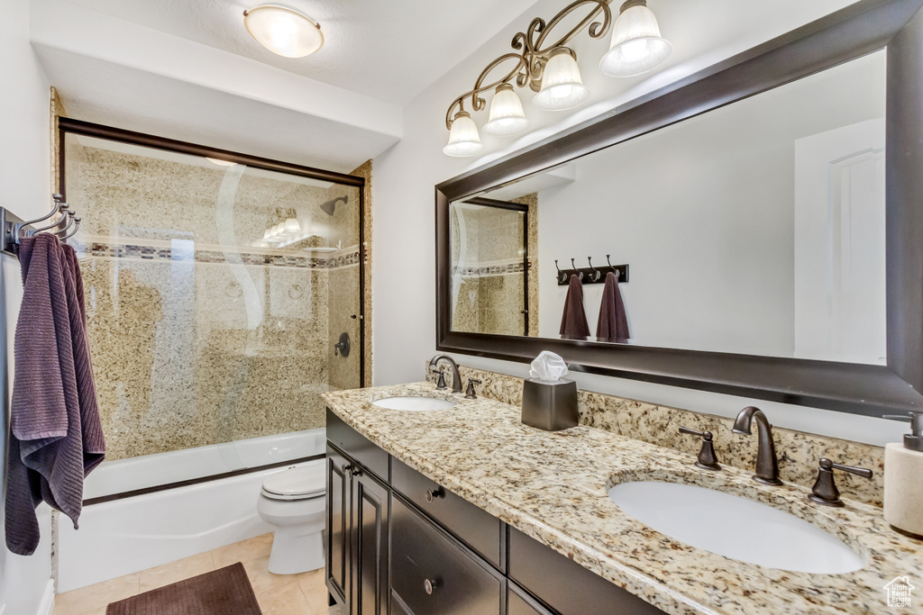 Full bathroom with dual bowl vanity, toilet, tile floors, and shower / bath combination with glass door