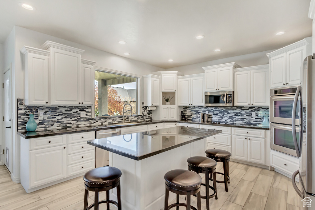 Kitchen featuring appliances with stainless steel finishes, a kitchen island, a breakfast bar area, backsplash, and white cabinetry