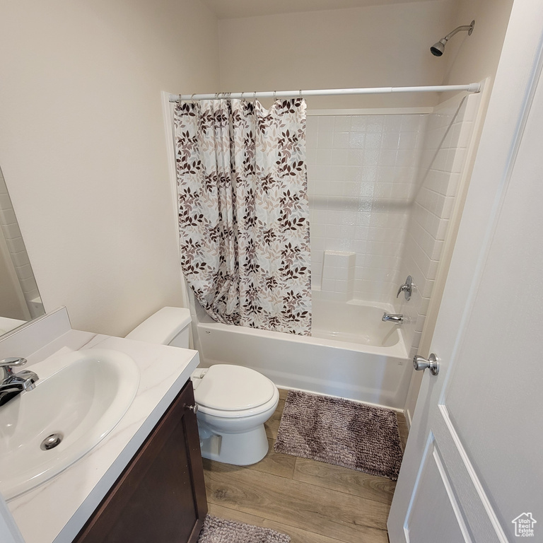 Full bathroom with oversized vanity, hardwood / wood-style flooring, toilet, and shower / bath combo with shower curtain