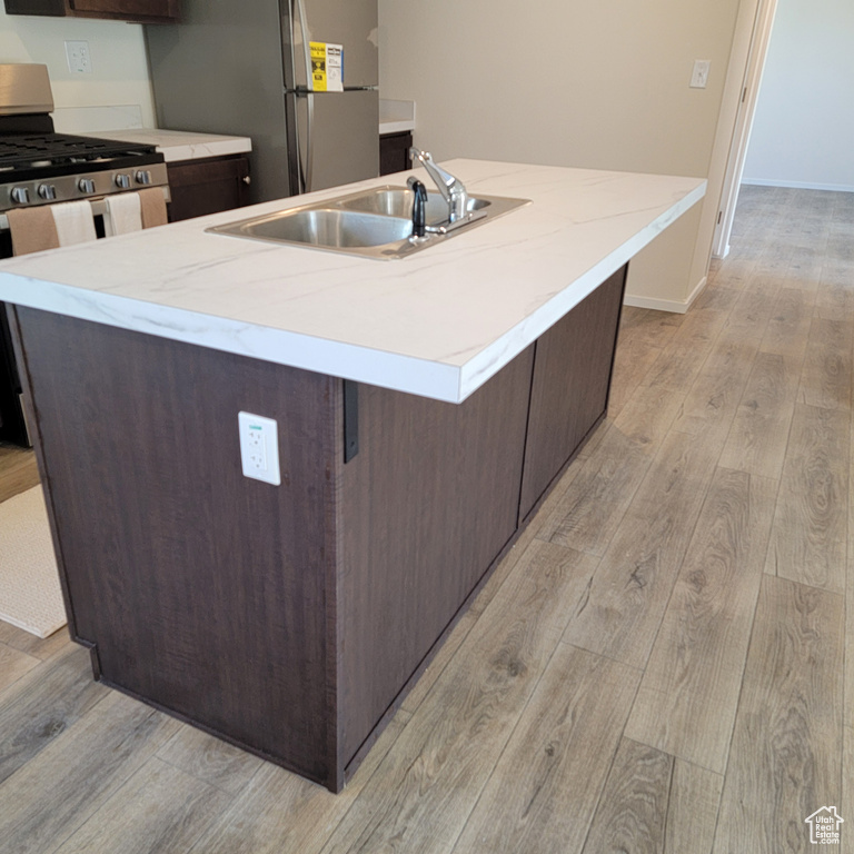Kitchen featuring sink, light hardwood / wood-style floors, an island with sink, and stainless steel appliances
