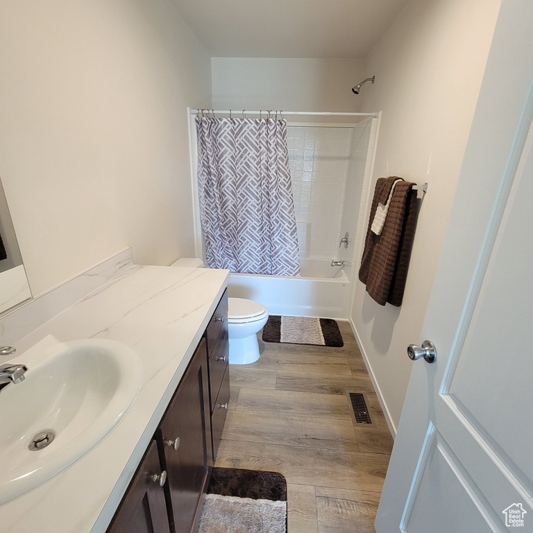 Full bathroom with hardwood / wood-style floors, vanity, toilet, and shower / bathtub combination with curtain