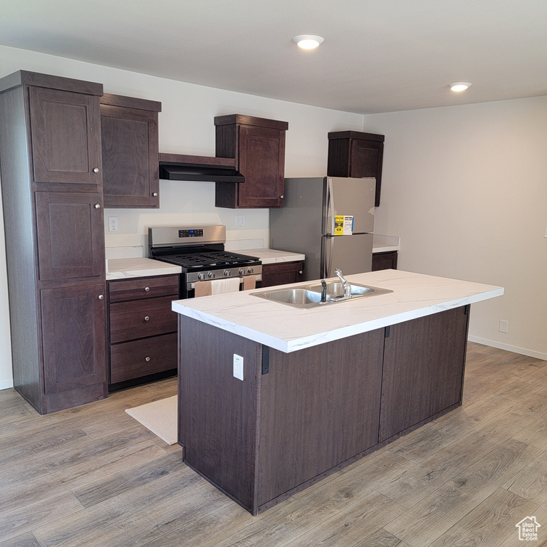 Kitchen with dark brown cabinetry, a center island with sink, light hardwood / wood-style flooring, and stainless steel appliances