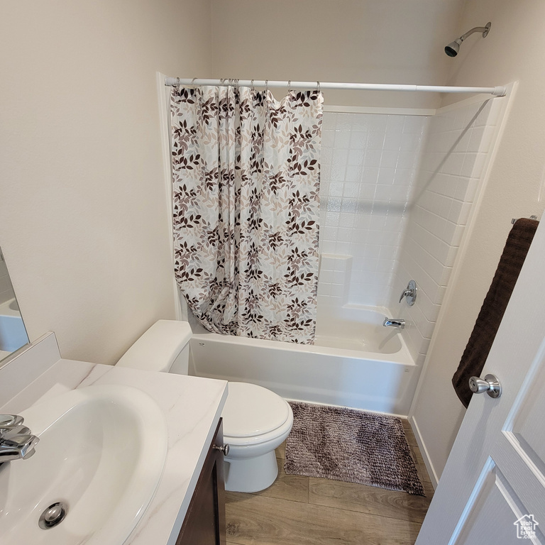 Full bathroom with wood-type flooring, large vanity, toilet, and shower / bath combo with shower curtain