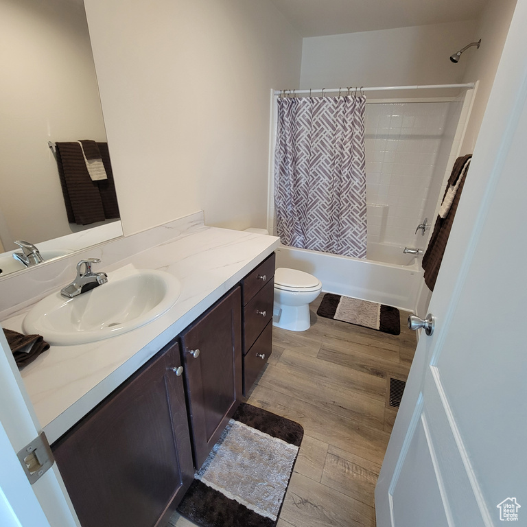 Full bathroom featuring toilet, vanity, shower / bathtub combination with curtain, and hardwood / wood-style flooring