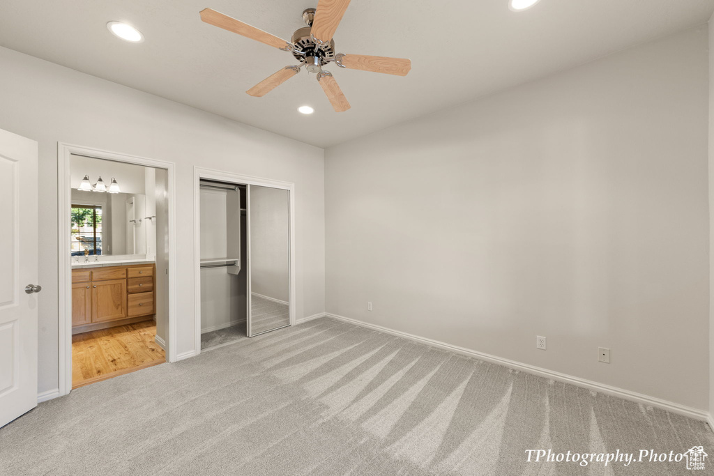 Unfurnished bedroom featuring a closet, ensuite bath, ceiling fan, and light carpet