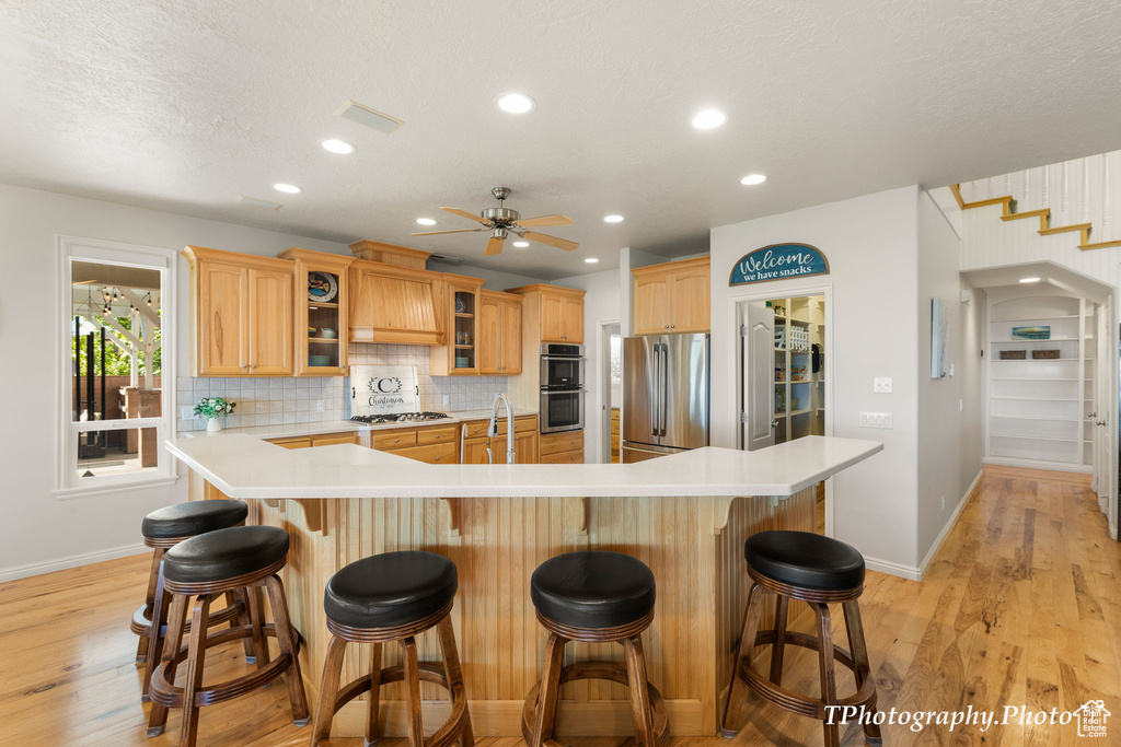 Kitchen featuring a center island with sink, stainless steel appliances, a kitchen bar, and light wood-type flooring