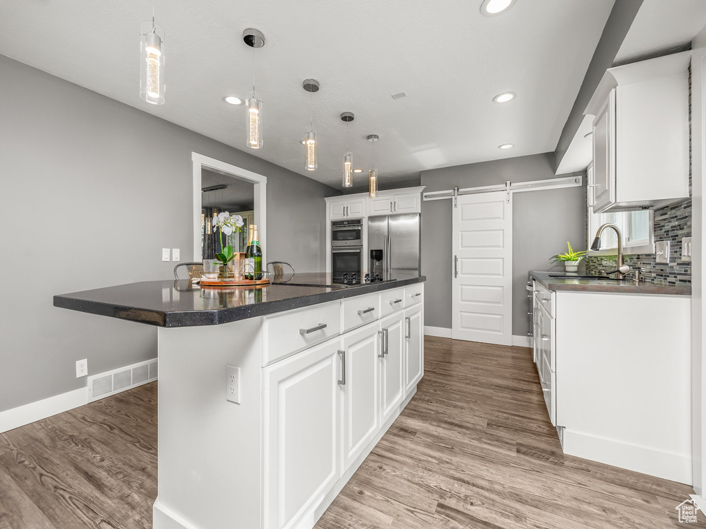 Kitchen with decorative light fixtures, appliances with stainless steel finishes, and white cabinetry