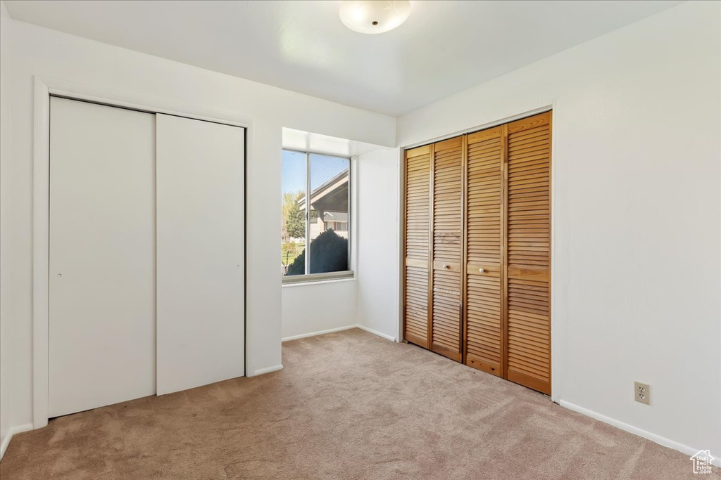 Unfurnished bedroom featuring light carpet and two closets