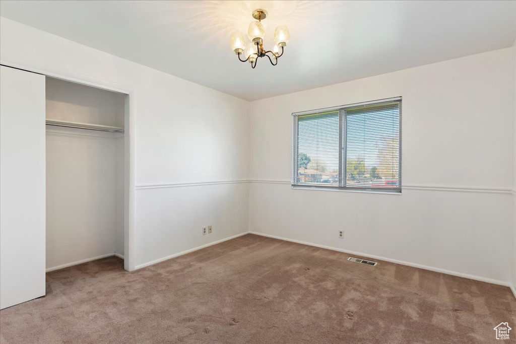 Unfurnished bedroom with light colored carpet, a closet, and an inviting chandelier