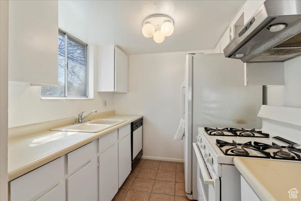 Kitchen featuring white appliances, white cabinetry, wall chimney range hood, sink, and light tile floors
