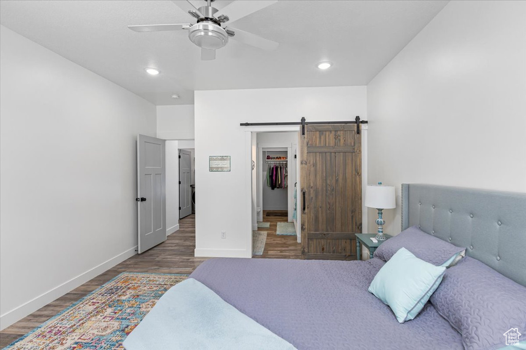 Bedroom with a barn door, dark hardwood / wood-style flooring, and ceiling fan