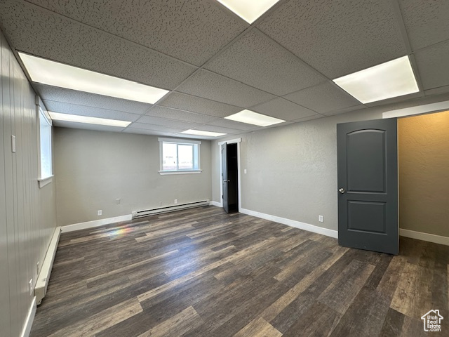 Basement featuring a drop ceiling, baseboard heating, and dark hardwood / wood-style flooring