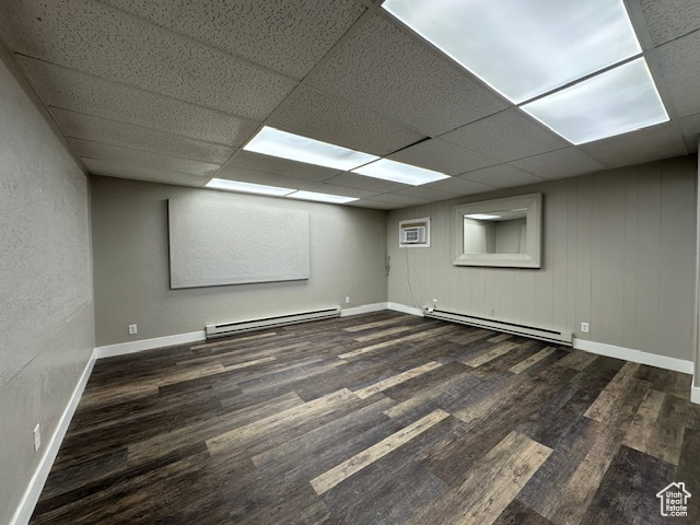 Empty room with dark hardwood / wood-style floors, a drop ceiling, and a baseboard heating unit