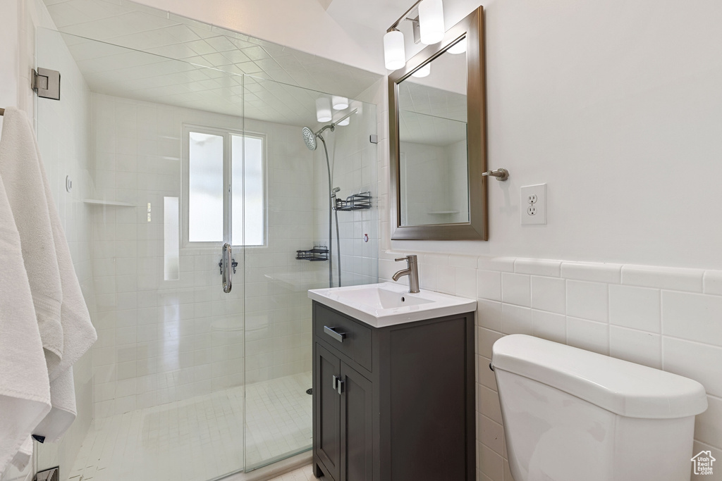 Bathroom featuring walk in shower, vanity, toilet, and tile walls