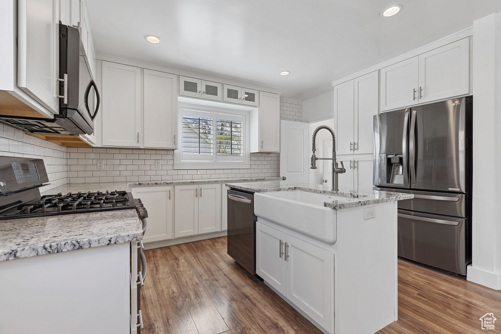 Kitchen with appliances with stainless steel finishes, dark hardwood / wood-style flooring, a kitchen island with sink, and white cabinetry
