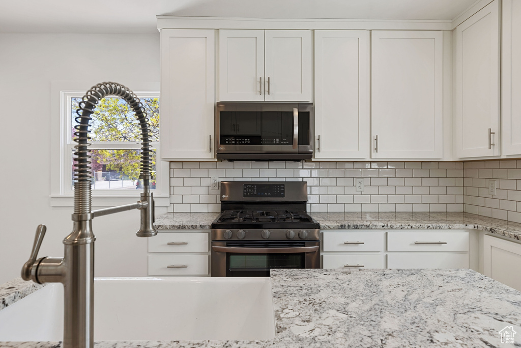 Kitchen with appliances with stainless steel finishes, tasteful backsplash, light stone countertops, and white cabinets