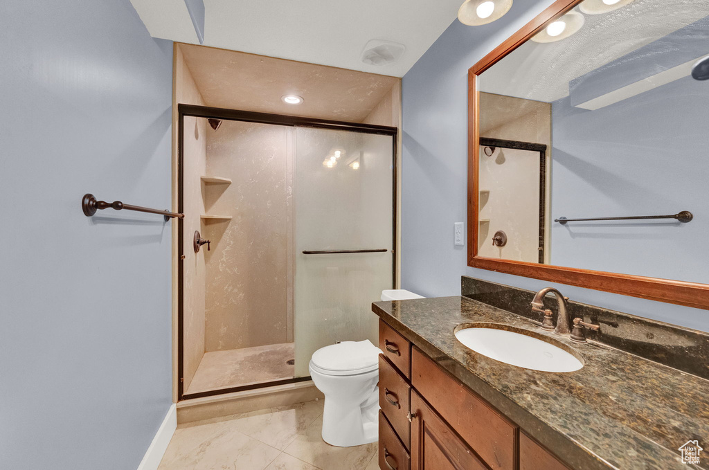 Bathroom with tile flooring, a shower with door, vanity with extensive cabinet space, and toilet