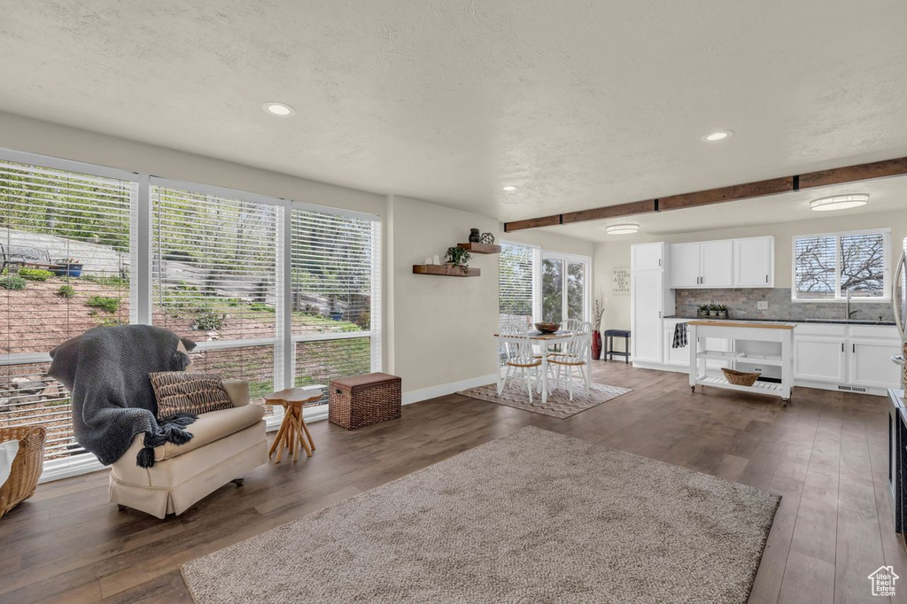Living room featuring plenty of natural light, beam ceiling, and dark wood-type flooring