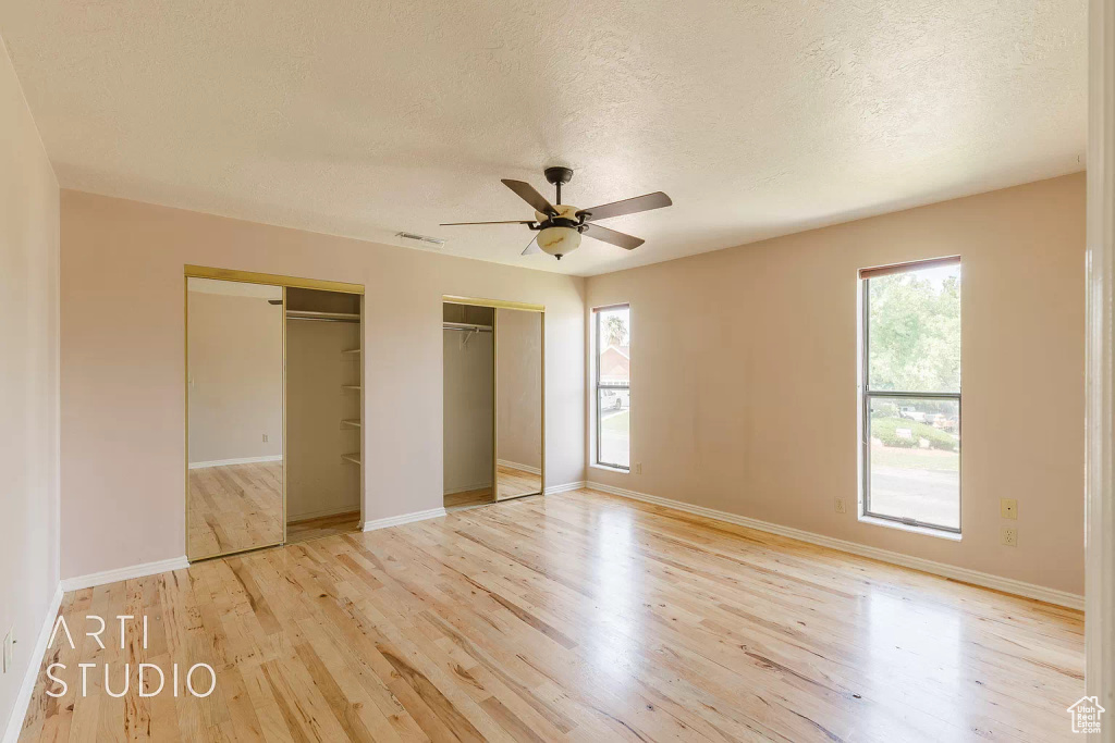 Unfurnished bedroom with a textured ceiling, light hardwood / wood-style flooring, ceiling fan, and multiple closets