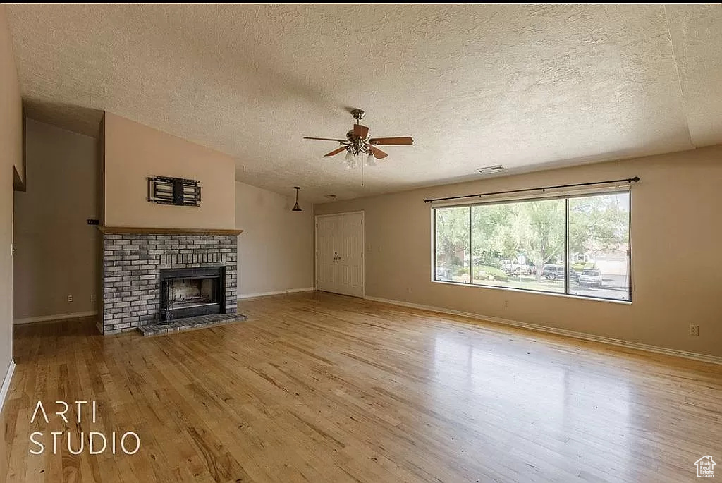 Unfurnished living room with a textured ceiling, ceiling fan, light wood-type flooring, and a brick fireplace