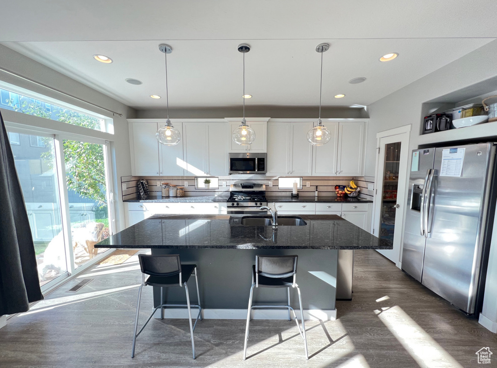 Kitchen with stainless steel appliances, a kitchen island with sink, dark stone countertops, white cabinets, and dark hardwood / wood-style flooring