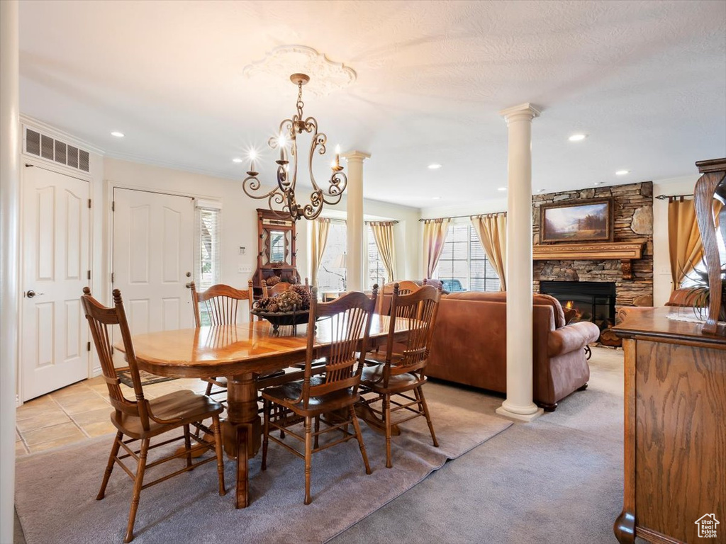 Carpeted dining room with an inviting chandelier, decorative columns, a stone fireplace, and plenty of natural light