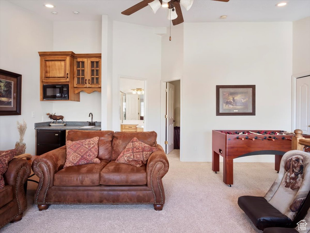 Carpeted living room with ceiling fan, sink, and a towering ceiling