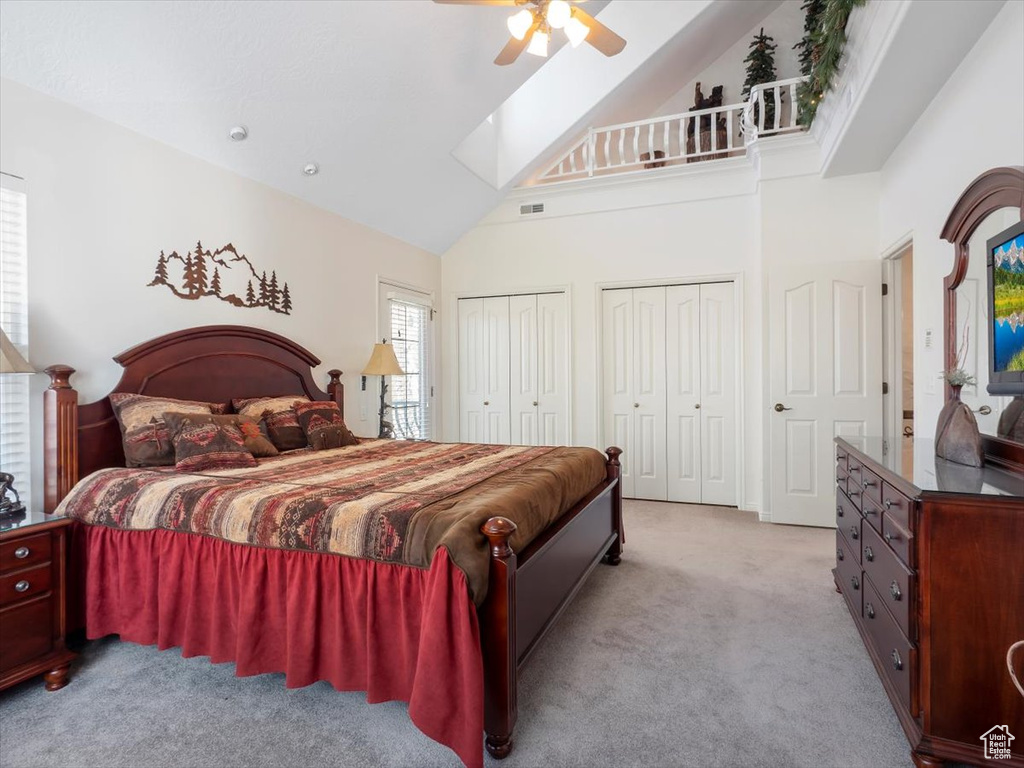 Carpeted bedroom featuring ceiling fan, two closets, and high vaulted ceiling