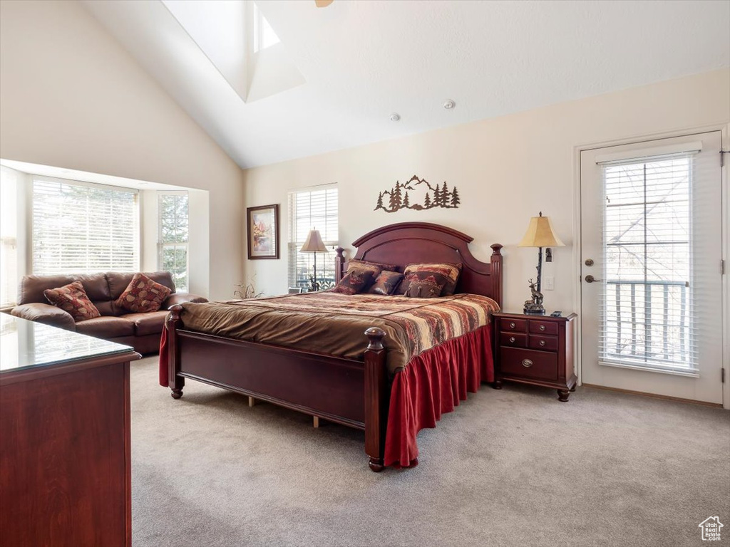 Carpeted bedroom featuring high vaulted ceiling, access to exterior, a skylight, and multiple windows