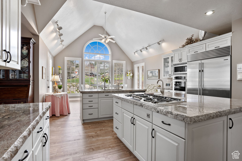 Kitchen featuring ceiling fan, rail lighting, white cabinetry, and built in appliances