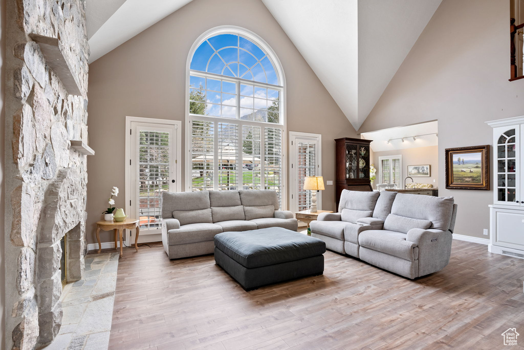 Living room with light hardwood / wood-style flooring, high vaulted ceiling, and a stone fireplace