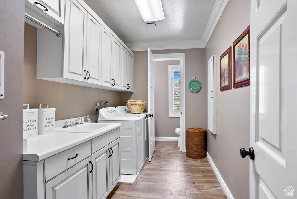 Clothes washing area with washing machine and dryer, cabinets, light hardwood / wood-style floors, crown molding, and washer hookup