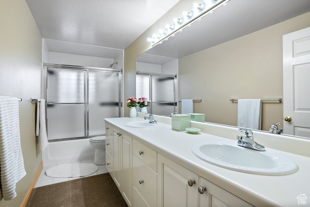 Full bathroom featuring double vanity, combined bath / shower with glass door, toilet, and tile flooring