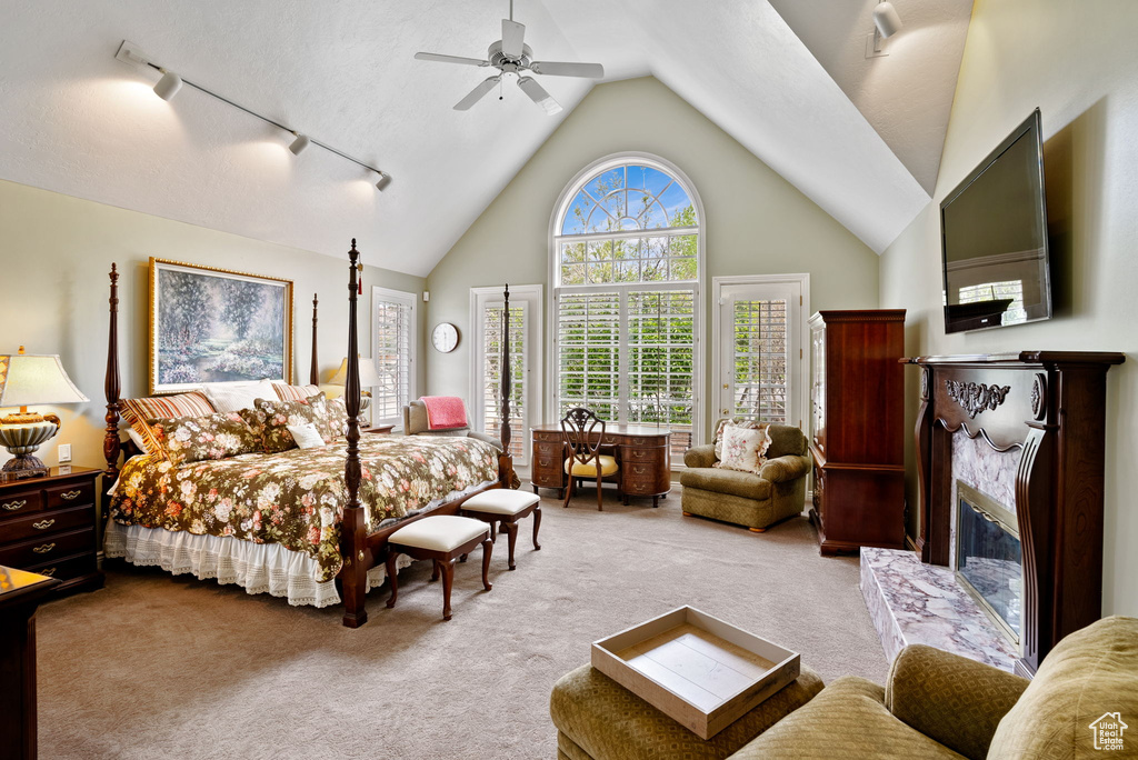 Bedroom featuring light colored carpet, high vaulted ceiling, ceiling fan, a high end fireplace, and rail lighting