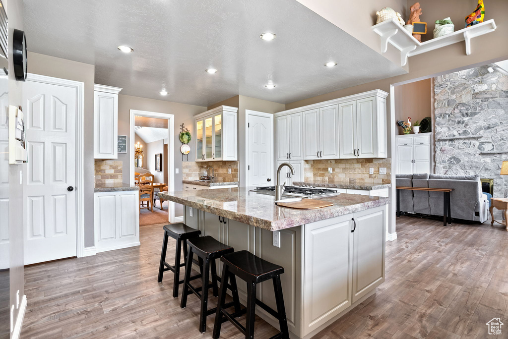 Kitchen with tasteful backsplash, light hardwood / wood-style flooring, white cabinets, and light stone countertops