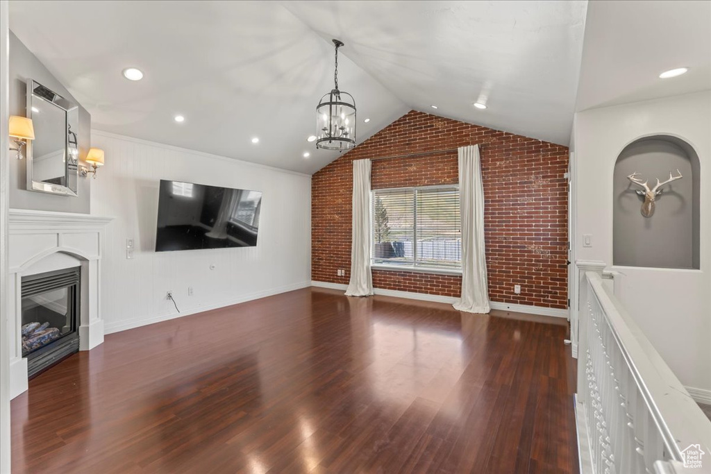 Unfurnished living room with a notable chandelier, brick wall, vaulted ceiling, and dark hardwood / wood-style floors