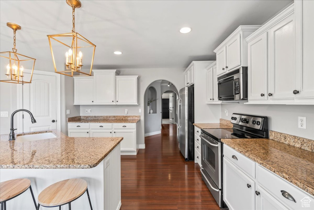 Kitchen featuring appliances with stainless steel finishes, hanging light fixtures, dark hardwood / wood-style floors, white cabinetry, and sink